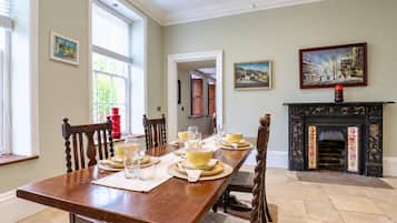 Une salle à manger avec une longue table en bois, dressée pour six personnes, entourée de chaises, et agrémentée d’une cheminée et d’œuvres d’art aux murs.