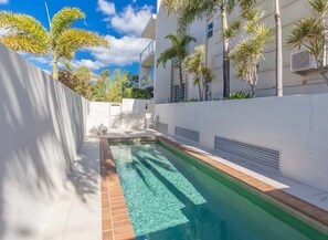 A swimming pool with clear water, surrounded by a white wall and palm trees. - Good Company by Aryve (Mermaid Beach)