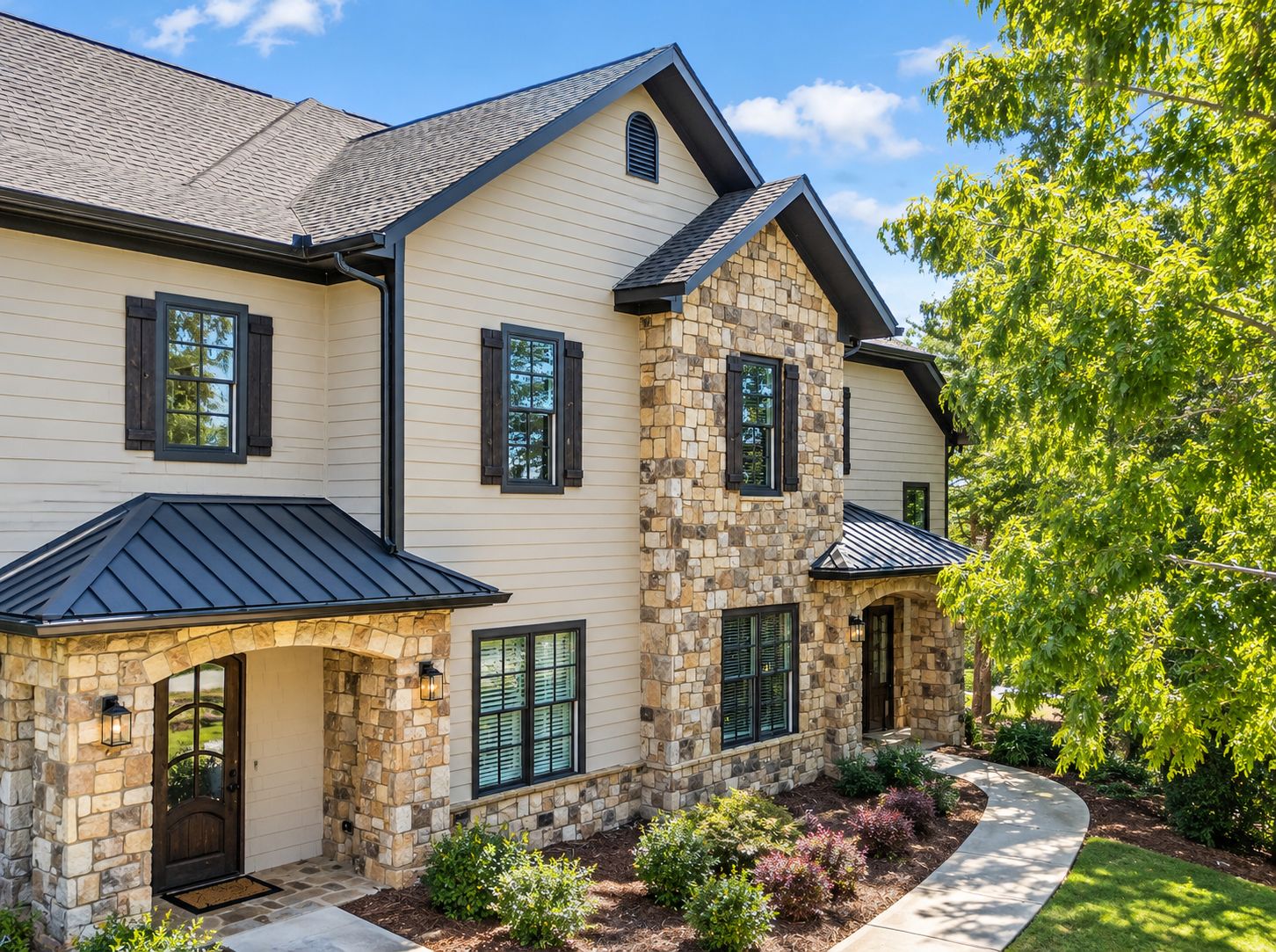 A two-story house with a stone facade, a dark roof, and a landscaped front yard.