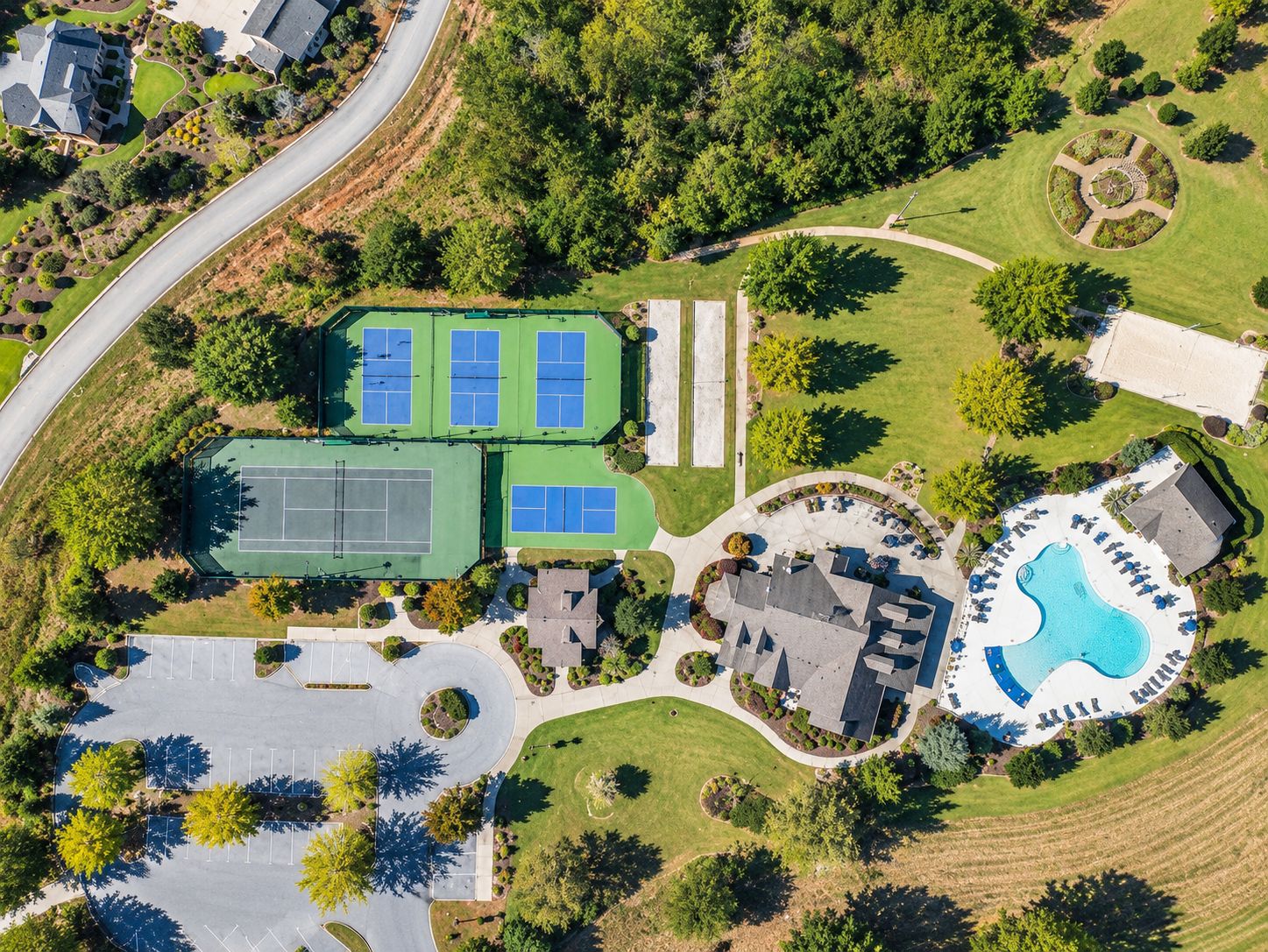 An aerial view of a residential area with a tennis court, a swimming pool, and a parking lot.