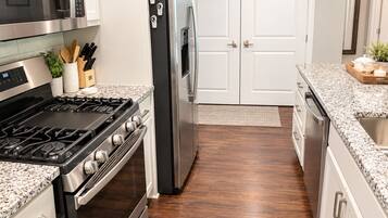 A modern kitchen with stainless steel appliances, a granite countertop, and wooden flooring.