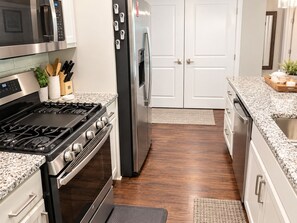 A modern kitchen with stainless steel appliances, a granite countertop, and wooden flooring.