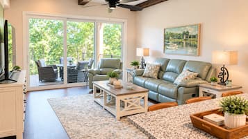 A spacious living area with a sofa, coffee table, and dining table. There is a sliding glass door leading to an outdoor patio.