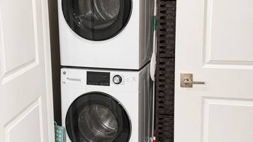 A laundry room with two stacked front-loading washing machines, a wicker basket on top, and a door with a dark patterned frame.