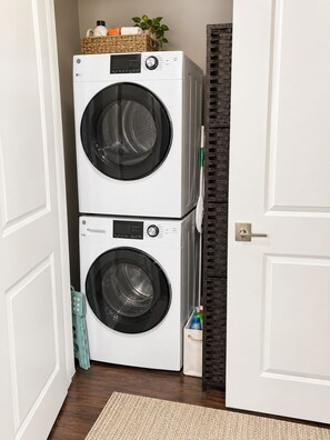 A laundry room with two stacked front-loading washing machines, a wicker basket on top, and a door with a dark patterned frame.