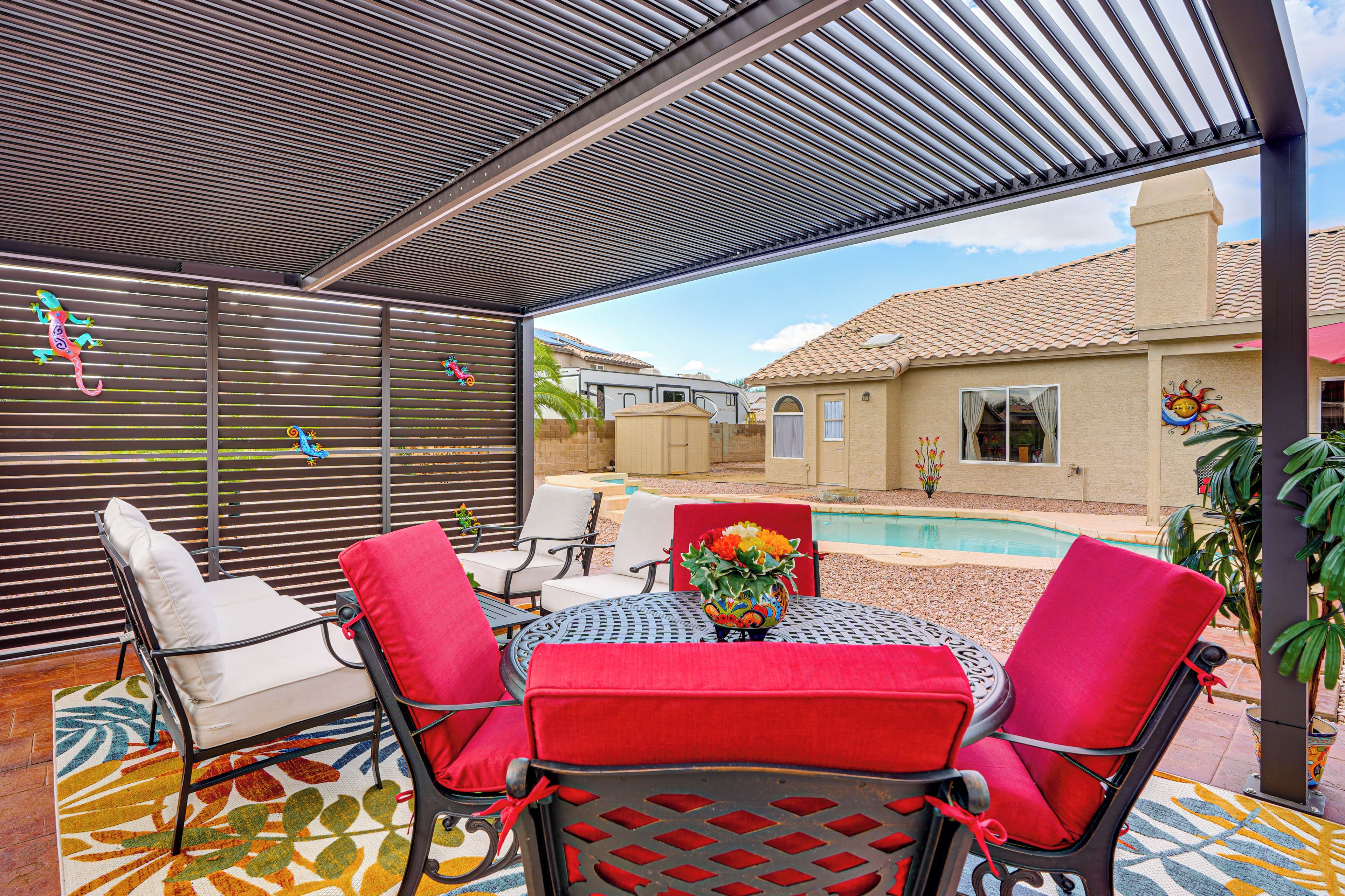 An outdoor patio with a pool, covered seating, and a decorative wall.