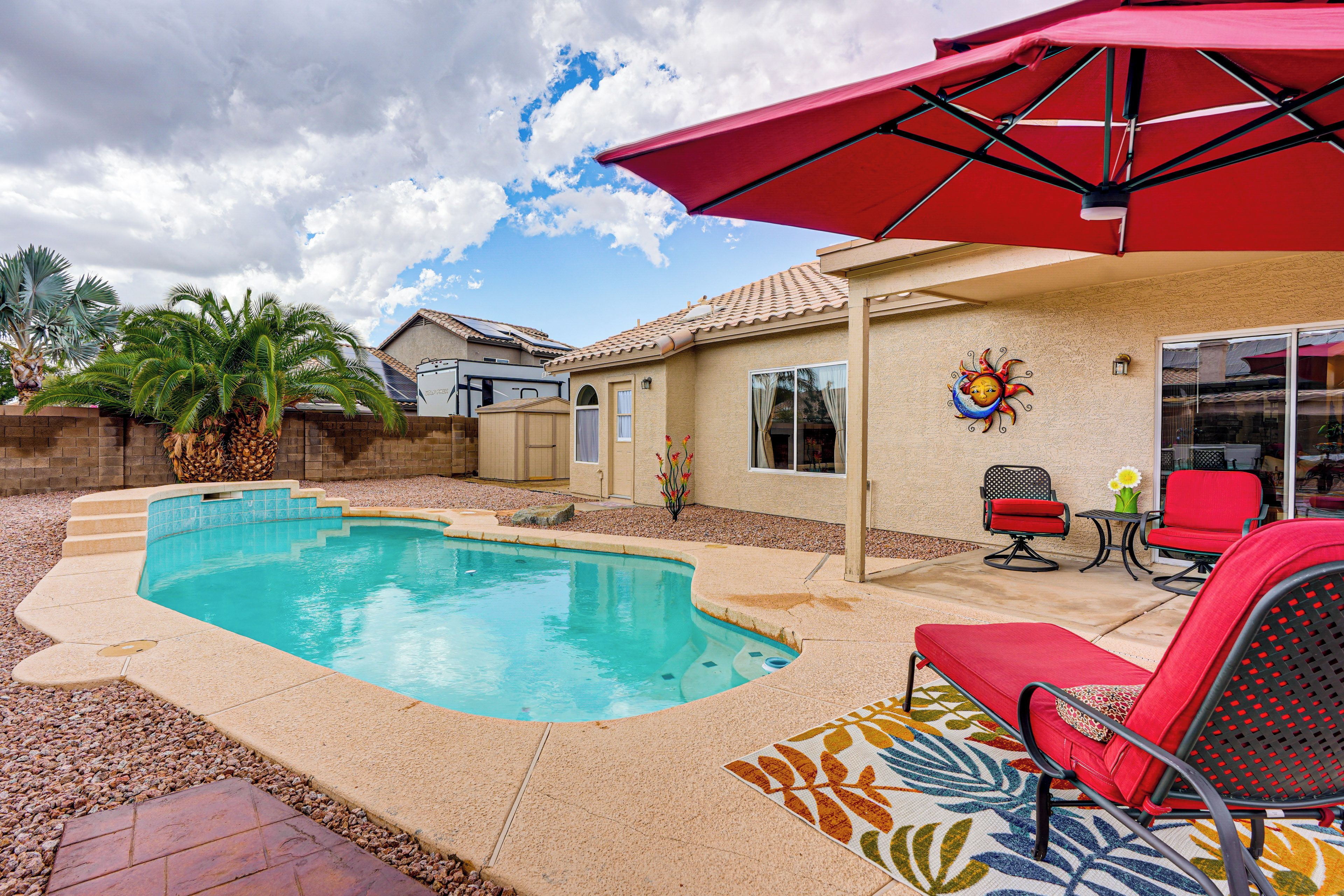 A backyard with a swimming pool, patio furniture, and a red umbrella.