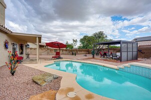 A backyard with a swimming pool, patio furniture, and a covered seating area.