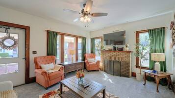 A living room with a fireplace, a ceiling fan, and a television.