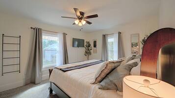 A bedroom with a bed, a ceiling fan, a TV, and a window with curtains.