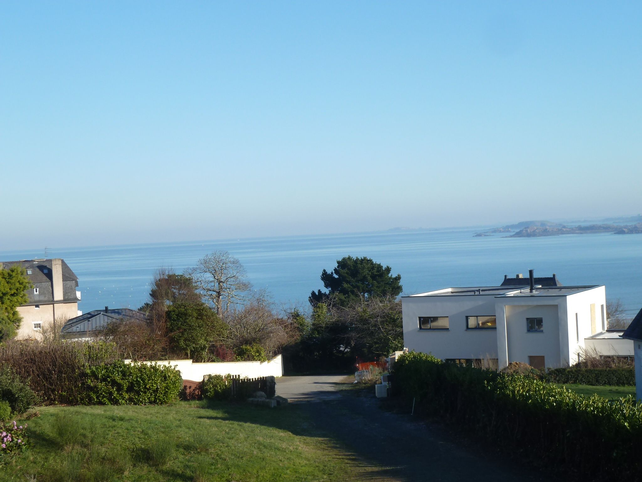 A residential area with a clear view of the sea, a pathway leading to a white building, and surrounding greenery.