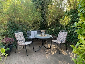 An outdoor patio with a round table and two chairs, surrounded by dense foliage. - Holiday Apartment With 1 Bedroom (Wyk auf Foehr)