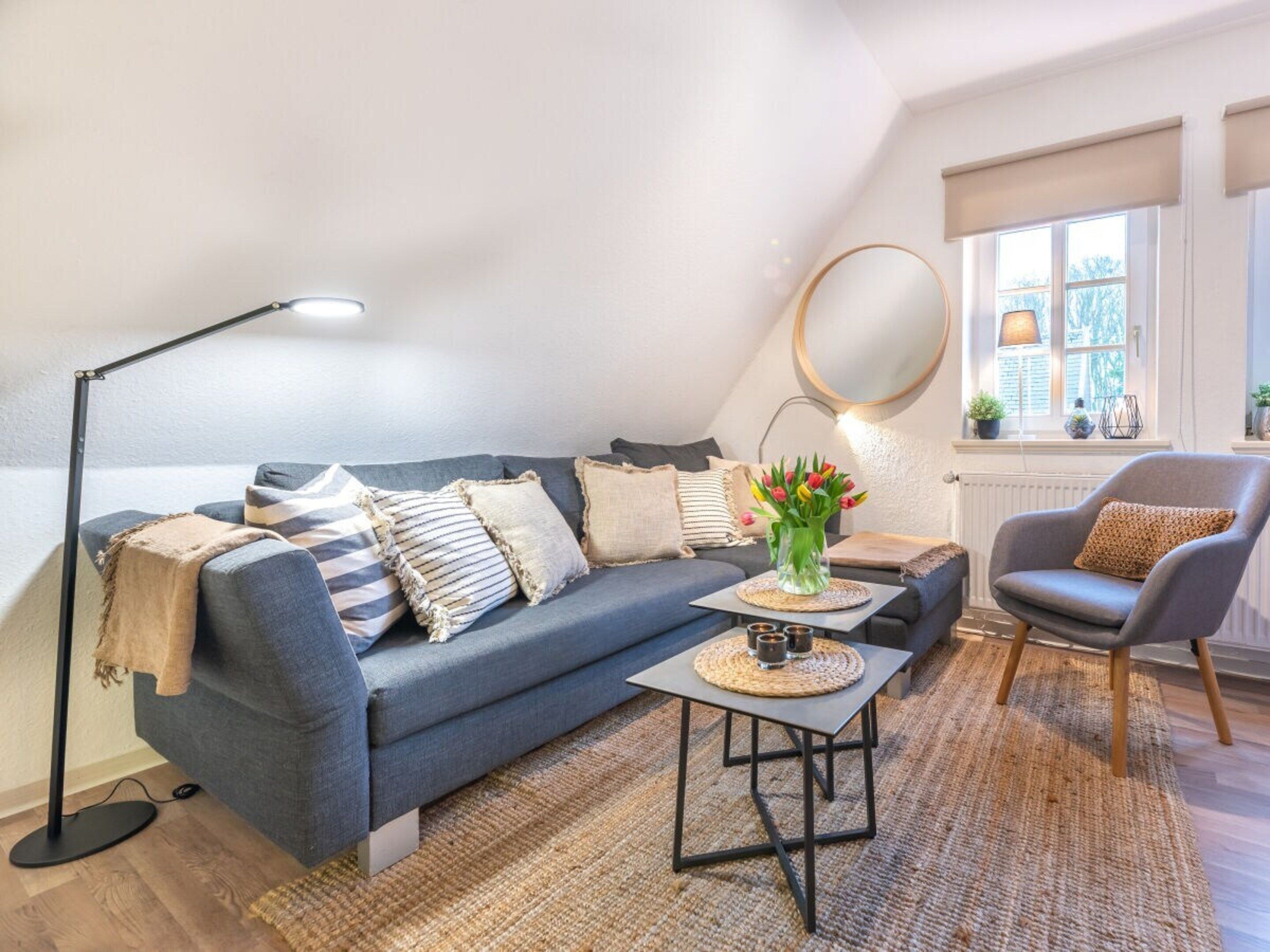 Un salon moderne avec un canapé, un fauteuil, une table basse, une lampe sur pied et un miroir au mur.