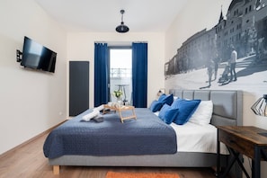 Ein modernes Schlafzimmer mit Bett, Flachbildfernseher, einem Fenster mit Vorhängen und einer Stadtszenen-Wandmalerei.
