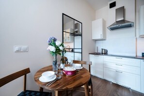 Eine moderne Küche mit weißen Schränken, einer Edelstahl-Dunstabzugshaube und einem Essbereich mit einem Holztisch, gedeckt für zwei Personen.
