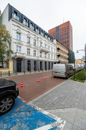 Eine Straße mit parkenden Autos, einem blauen Zebrastreifen und Gebäuden im Stil der klassischen und modernen Architektur.