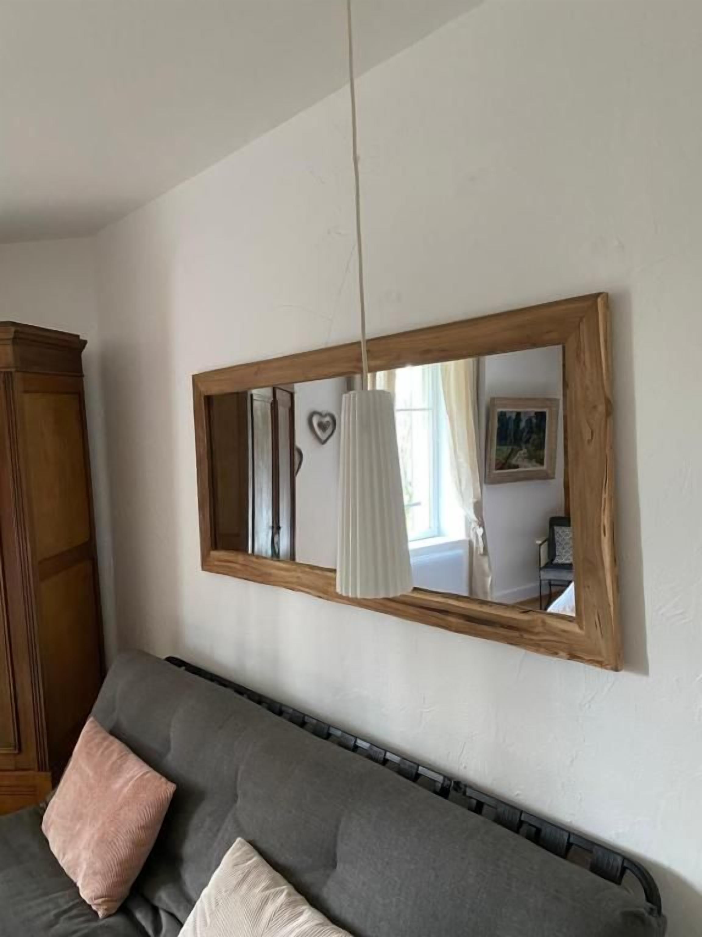 Una stanza con un divano grigio, un armadietto di legno e un grande specchio con cornice in legno.