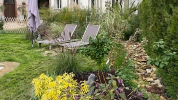 Un jardin avec une variété de plantes et de fleurs, un sentier et un bâtiment doté d’un balcon, visible au fond.