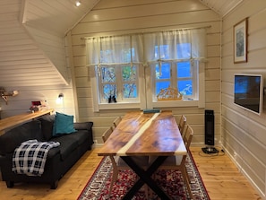 Ein gemütliches Zimmer mit einem Holztisch, einer schwarzen Couch und einem großen Fenster mit Vorhängen.