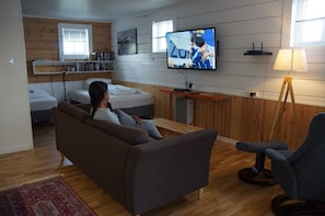 Ein modernes Wohnzimmer mit einer Couch, einem an der Wand befestigten Fernseher, einer Lampe und einem Bett mit einem Holz-Kopfstück.