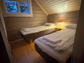 A small, cozy room with two beds, a window, and a nightstand with a lamp.