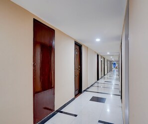 Un largo y estrecho pasillo de hotel con puertas a ambos lados, suelo de baldosas y una serie de luces en el techo.