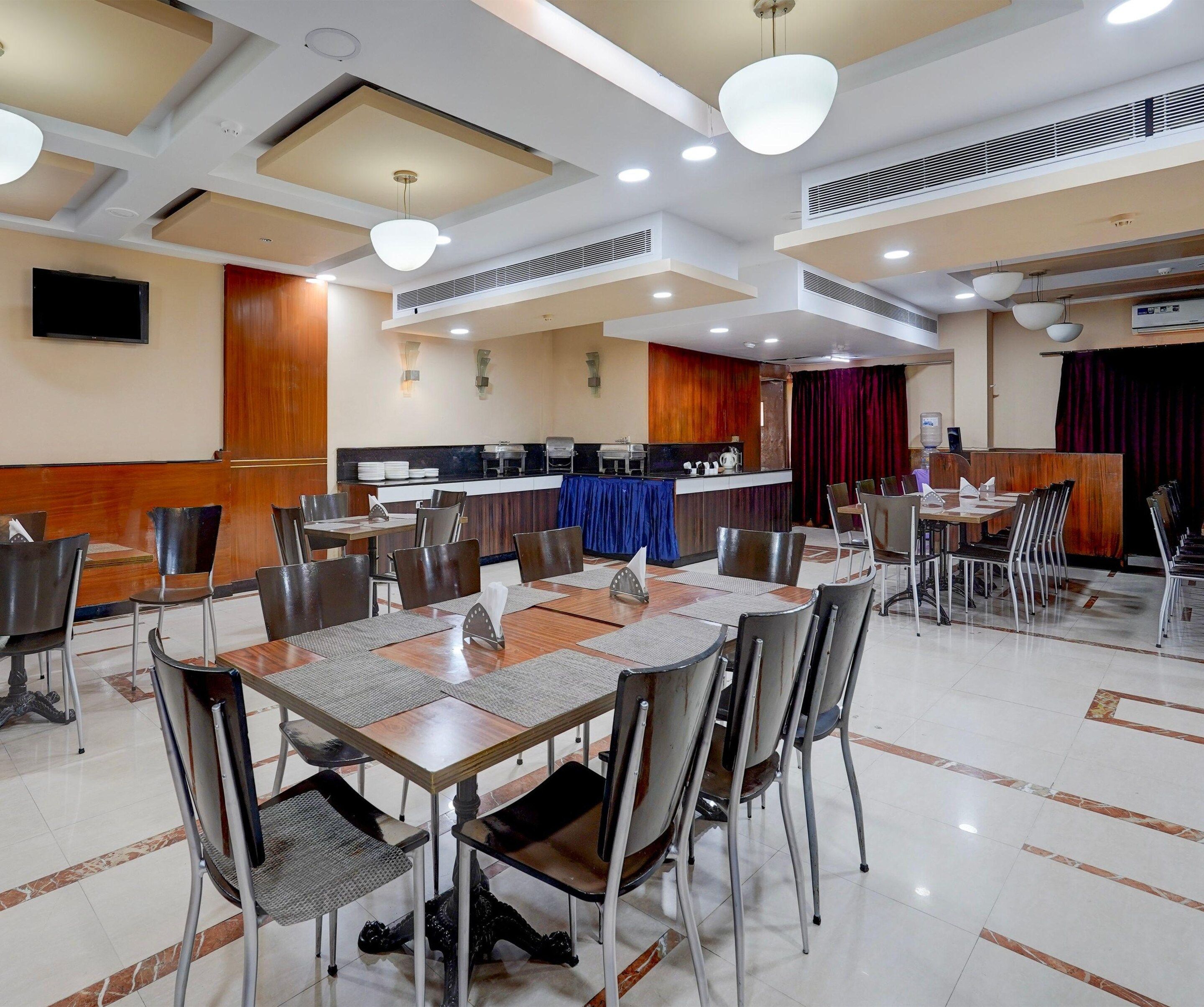 Comedor de hotel con varias mesas y sillas, una recepción y un dispensador de agua.