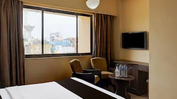 Habitación de hotel con cama, dos sillas, una mesita, televisión y ventana con cortinas.