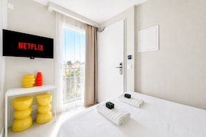 A hotel room with a bed, a television mounted on the wall, a small table with yellow and red objects, and a view of the outside through a door. - Secret Paradise near Disney & Paris - Netflix - 101 - 201 - 301 (Combs-la-Ville)