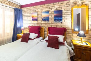 A double bed with red and white bedding, a brick wall, and three sunset paintings.