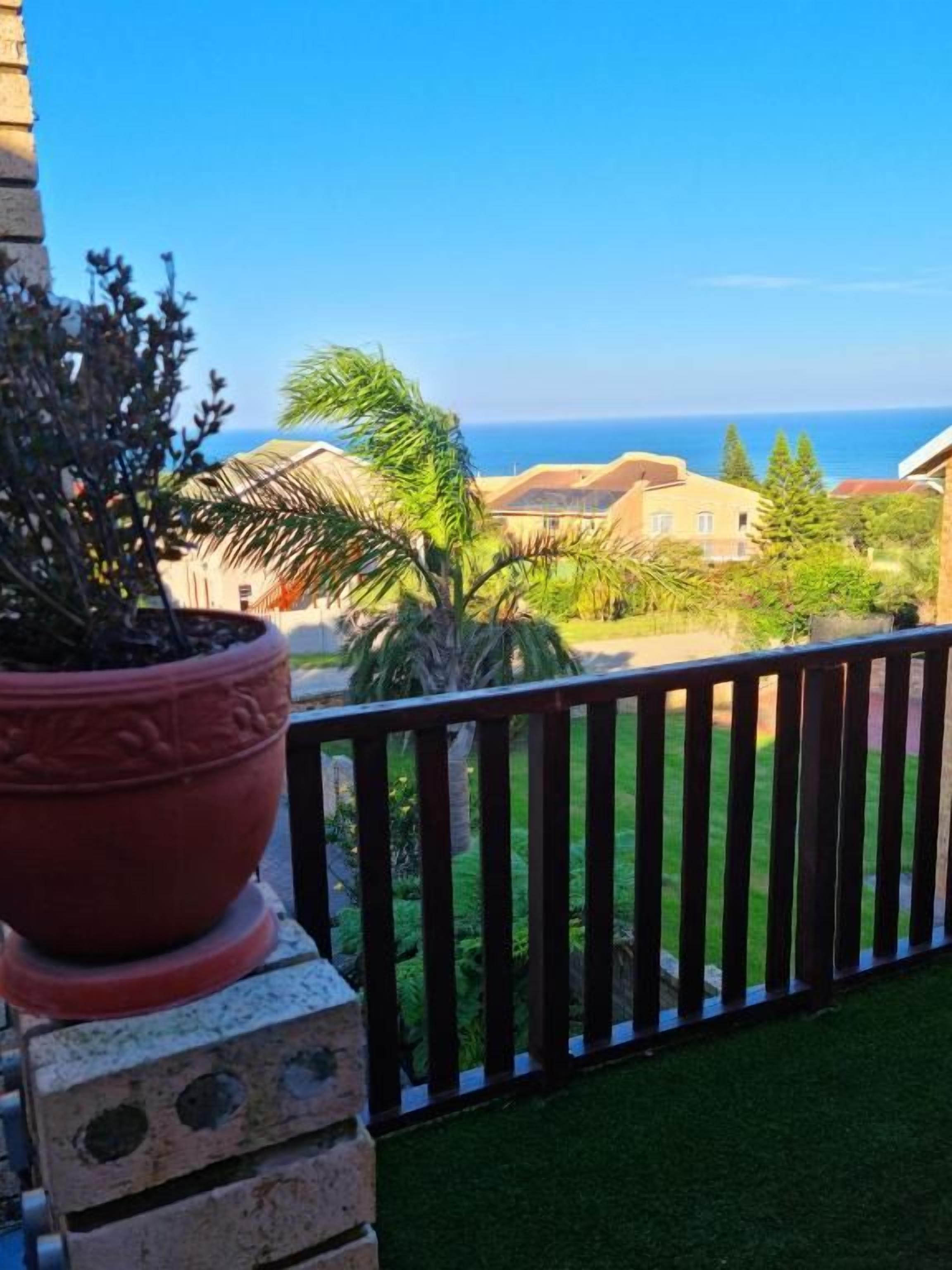 A balcony with a view of the sea, a potted plant, and a grassy area.