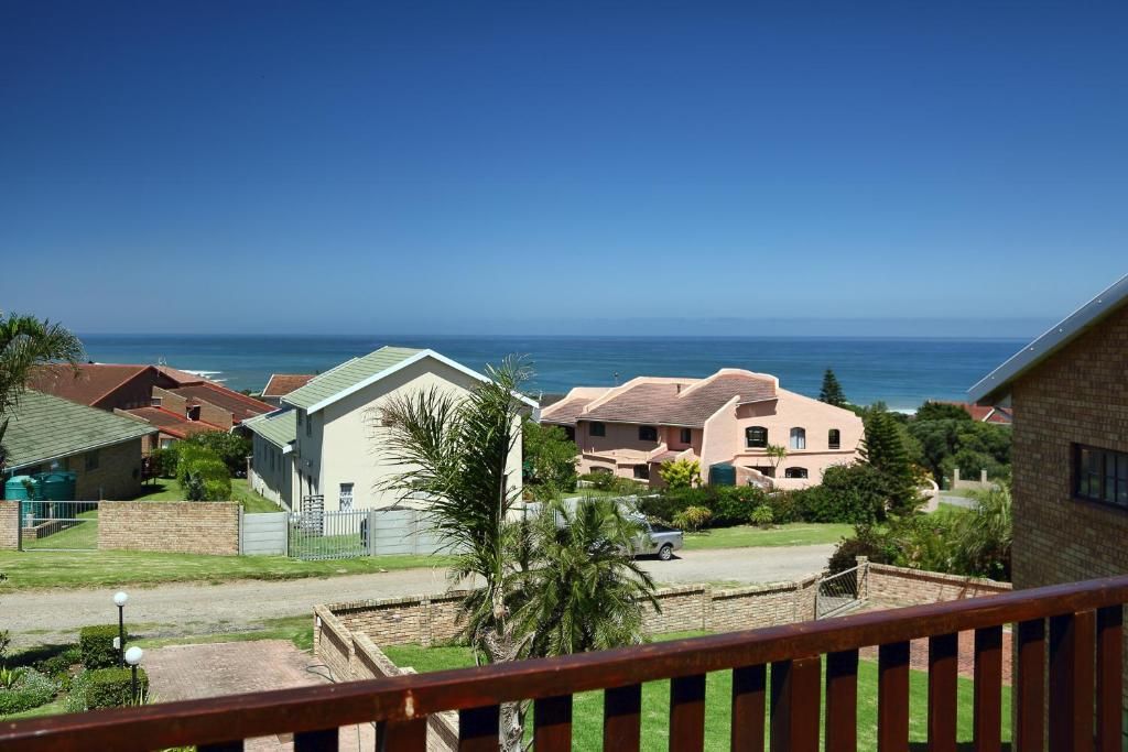 A residential area with houses, a clear view of the ocean, and a balcony with a railing.