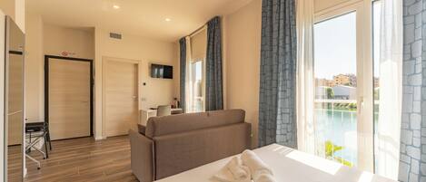 A hotel room with a bed, a sofa, a TV, a balcony with a view, and a door.