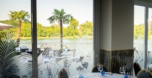 A dining area with a view of a lake and trees, featuring a table set with glasses and a white tablecloth. - Hotel Lagorá (San Giuliano Milanese)