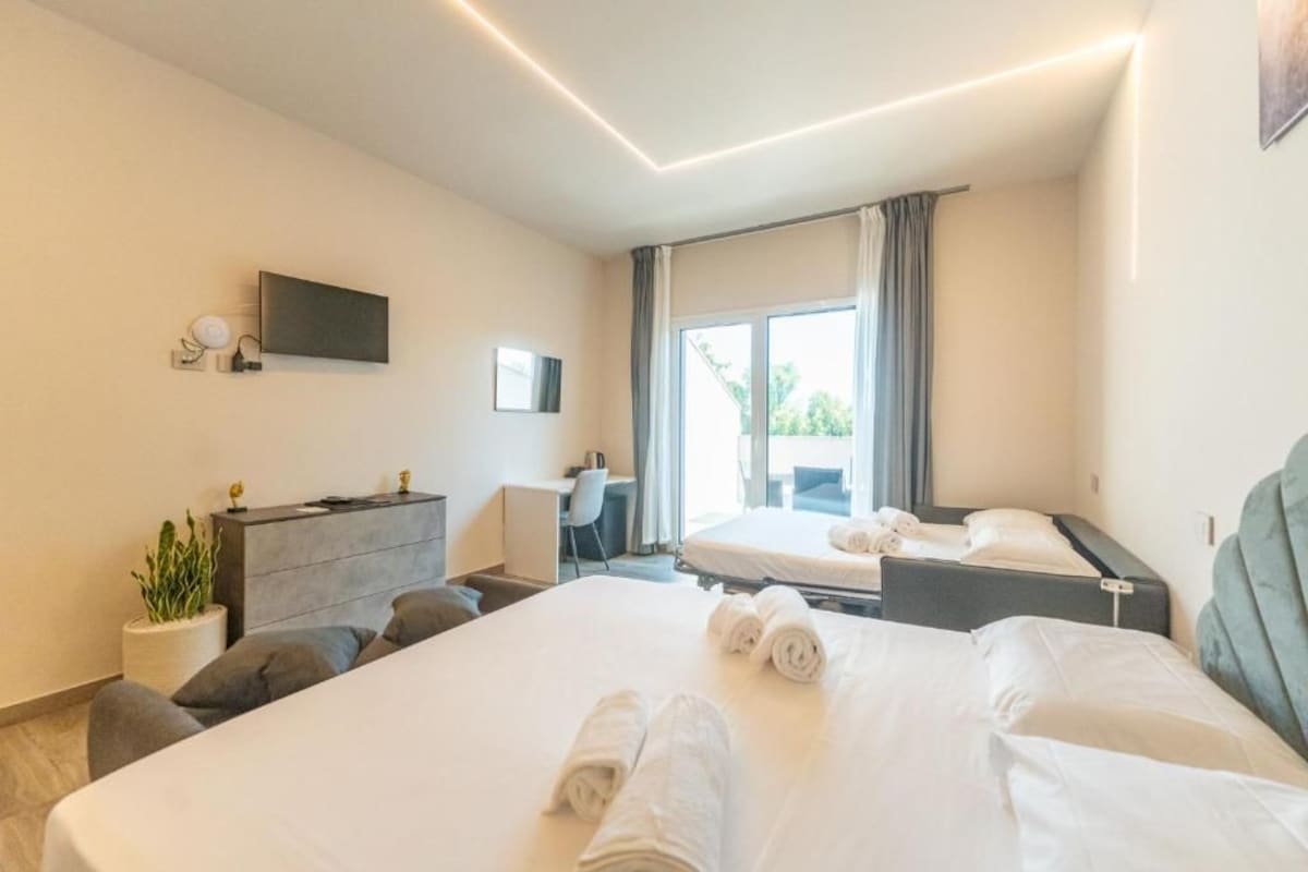 Ett hotellrum med en stor säng, ett skrivbord, en stol, en tv och ett fönster med gardiner.