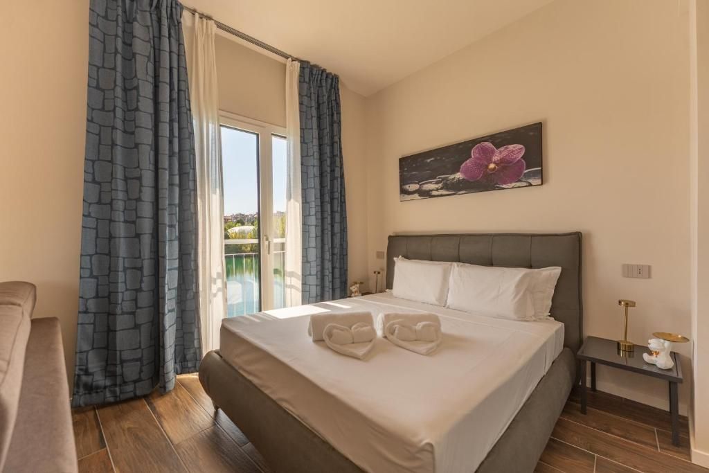 A hotel room with a bed, a nightstand, a painting, and a view through a window.
