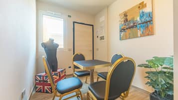 Una habitación pequeña con una mesa, cuatro sillas, un maniquí, una ventana y un cuadro en la pared.