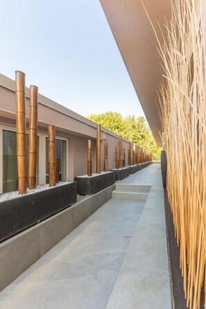 A modern building with a series of vertical bamboo structures, a flat roof, and a pathway leading to a seating area. - Hotel Lagorá (San Giuliano Milanese)