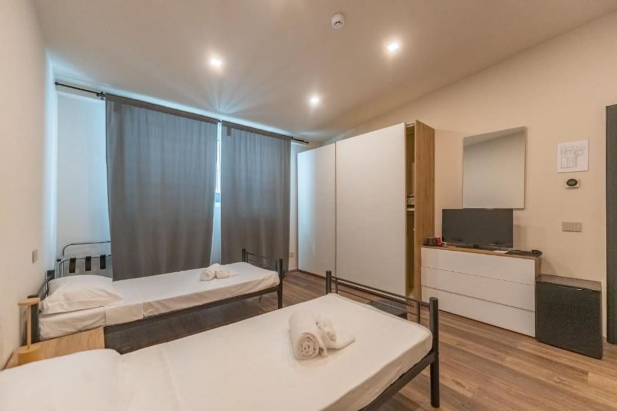 Una habitación de hotel con dos camas individuales, un televisor, un aparador y un espejo.