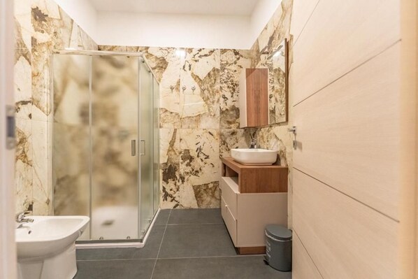 A bathroom with a glass shower enclosure, a white sink, and a wooden vanity. - Hotel Lagorá (San Giuliano Milanese)