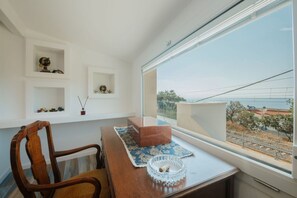 A room with a wooden dining table, a chair, a window with a view of the outside, and shelves with decorative items. - Capovillas - Villa Vittoria with pool and ocean view (Coccorino)