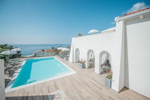 A rooftop swimming pool with a view of the sea, a covered seating area, and a white building with arches. - Capovillas - Villa Vittoria with pool and ocean view (Coccorino)