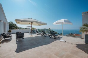 Een terras met lounge fauteuils en parasols, met uitzicht op de kust.
