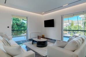 Un salon moderne avec une table basse en verre, des canapés blancs et un téléviseur à écran plat fixé au mur.