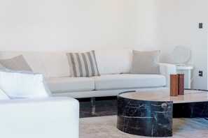 A modern living room with a white sofa, striped pillows, a round marble coffee table, and a small side table with decorative items. - 3 Bedroom Apartment at Glyfada’s Centre (Glyfada)