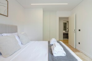 A modern hotel room with a large bed, a bedside table, a wardrobe, and a bathroom visible through an open door. - 3 Bedroom Apartment at Glyfada’s Centre (Glyfada)