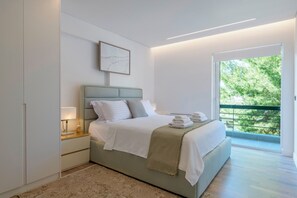 A modern bedroom with a bed, bedside tables, a nightstand, a framed picture, and a balcony with a view of trees. - 3 Bedroom Apartment at Glyfada’s Centre (Glyfada)