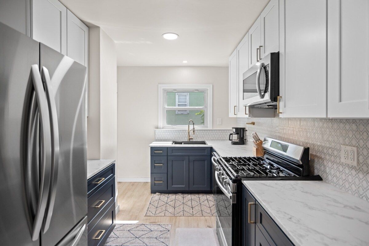 A modern kitchen with stainless steel appliances, dark cabinetry, and a patterned backsplash.
