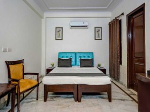 A hotel room with a bed, a chair, an air conditioning unit, and a wooden wardrobe. - Classic Sangam Vihar (Ghaziabad)