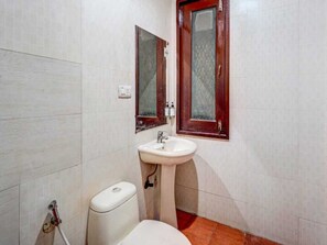 A bathroom with a white sink, a toilet, and a mirror with a wooden frame. - Classic Sangam Vihar (Ghaziabad)